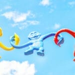 Yellow, blue and red plastic monkey toys have their arms linked together in front of a blue sky, symbolizing fun