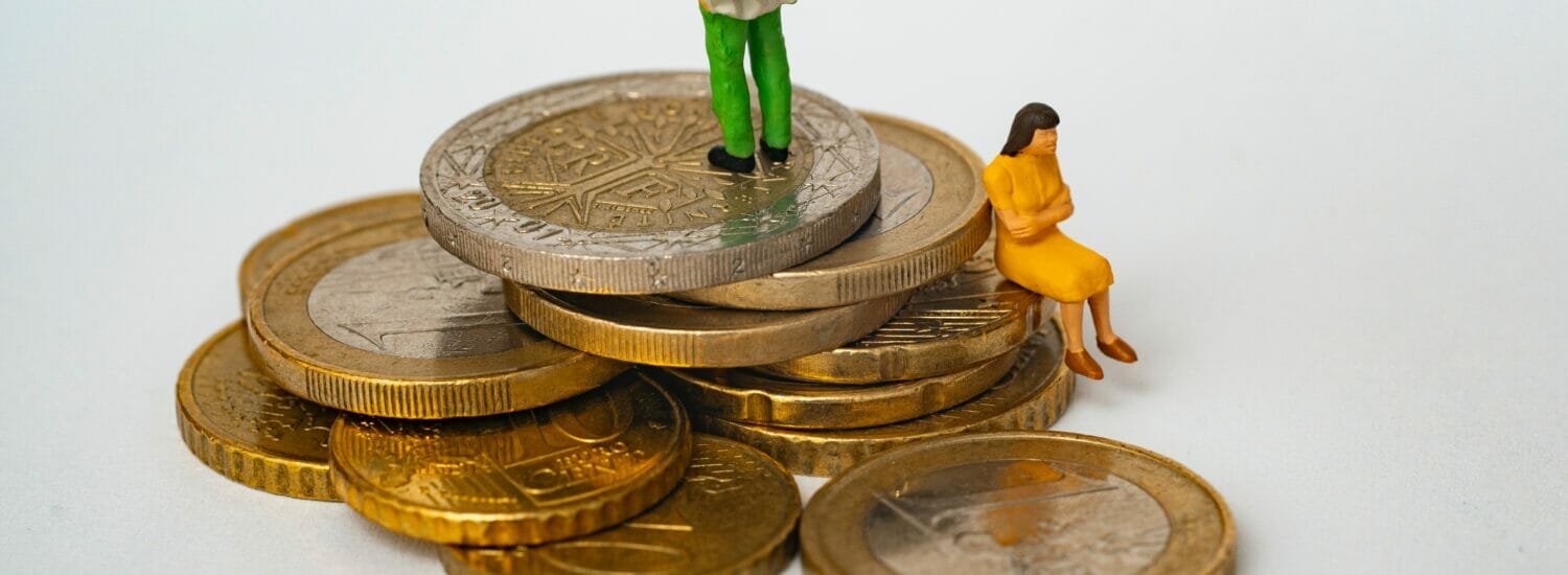 A pile of coins with a man figurine on top and a frustrated-looking woman figurine sitting on a lower level of coins