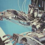 A robot made of silver metal playing a piano keyboard in front of a blue background