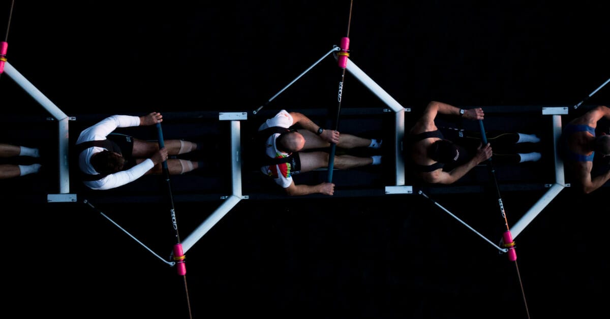 Collaborate: A crew team of four people rowing against a dark background