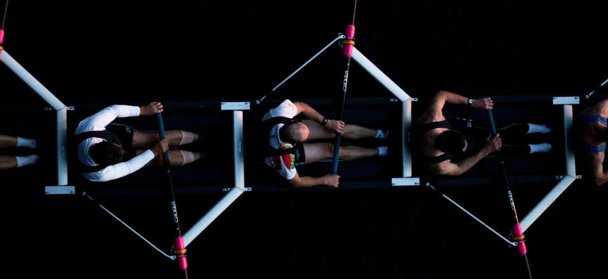 Collaborate: A crew team of four people rowing against a dark background