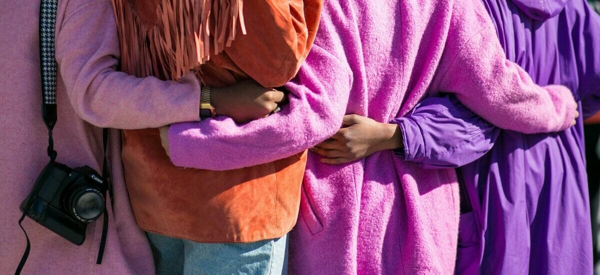 Four people in purple jackets holding hands behind each others backs, showing inclusion