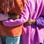 Four people in purple jackets holding hands behind each others backs, showing inclusion