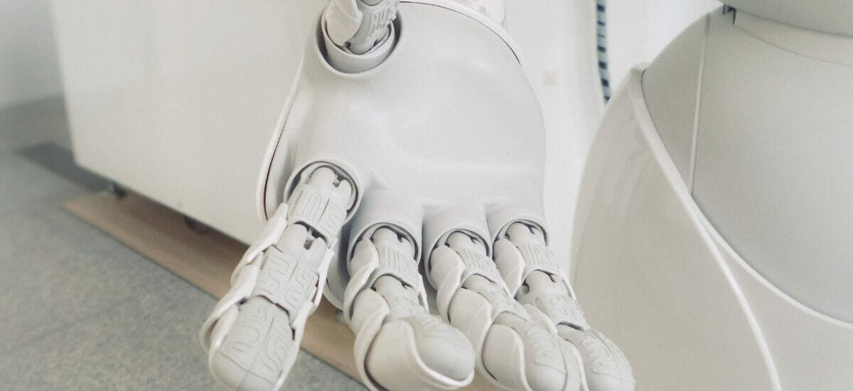 An image of a white robotic hand reaching out to the viewer in front of a white/gray background