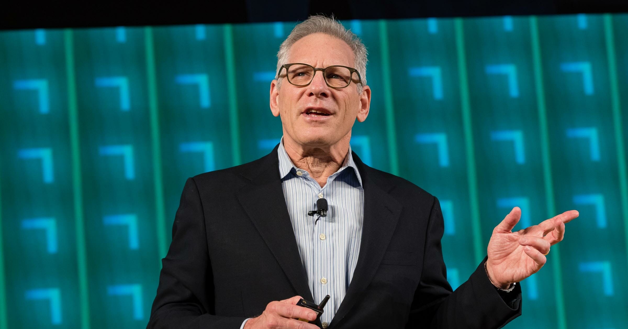 Image of Stew Friedman wearing a black suit jacket and light blue shirt in front of a teal blue background